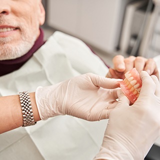 Dentist handing dentures to man in dental chair