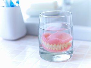 Complete set of dentures in a glass of clear fluid on a tiled countertop