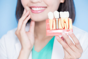 Dentist holding up model dental implant and touching her pearly white teeth